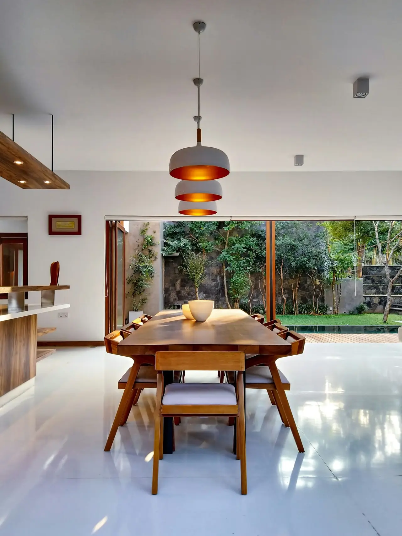 Dining table under copper pendants opening to a garden